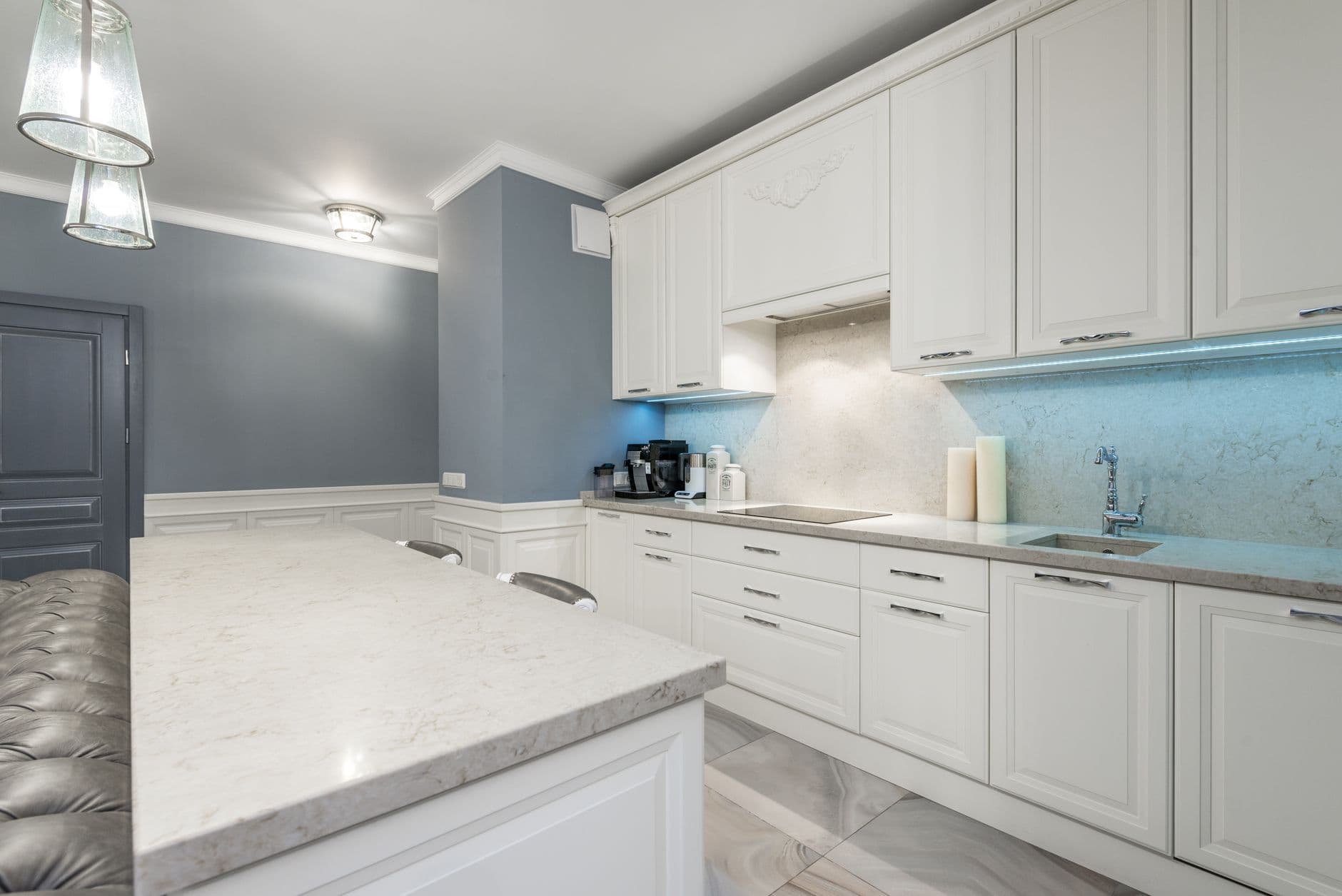 A kitchen with panelled white cabinetry, a pale marble-effect island worktop and pendant lights.