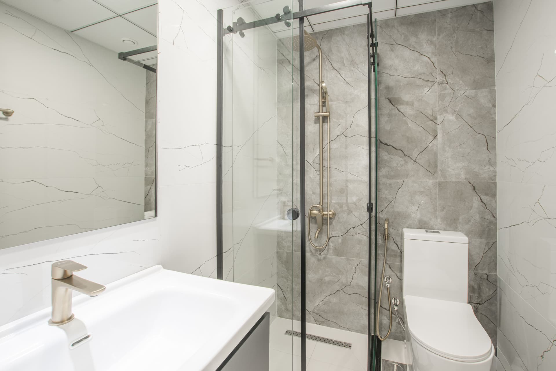 A bathroom with marble-effect wall tiling, a glass shower enclosure and a wall-hung vanity.