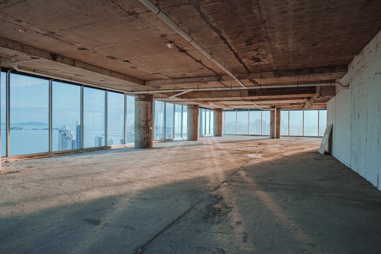 An empty commercial floor in shell condition, with exposed concrete, columns and floor-to-ceiling glazing.