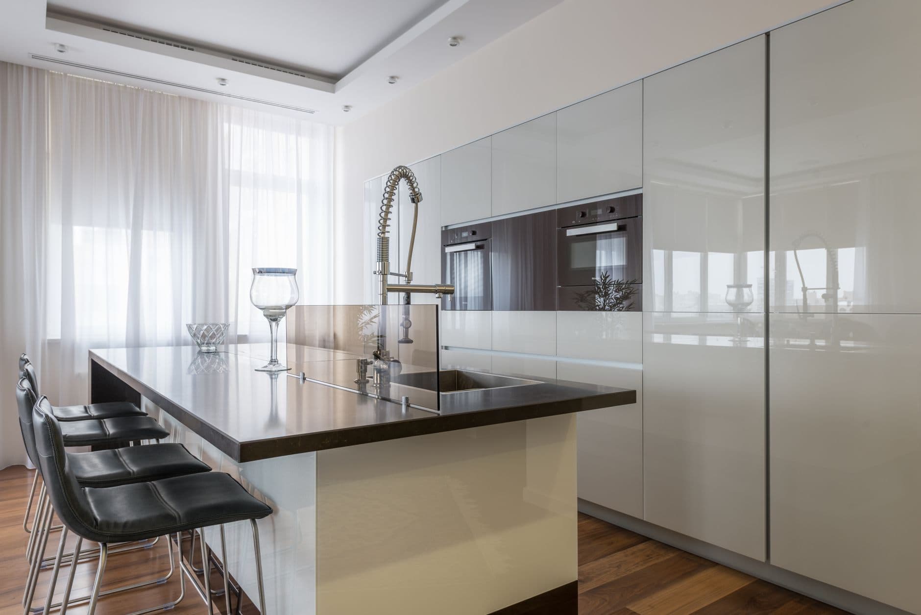 A modern kitchen with gloss white cabinetry, a dark stone island worktop and built-in ovens.