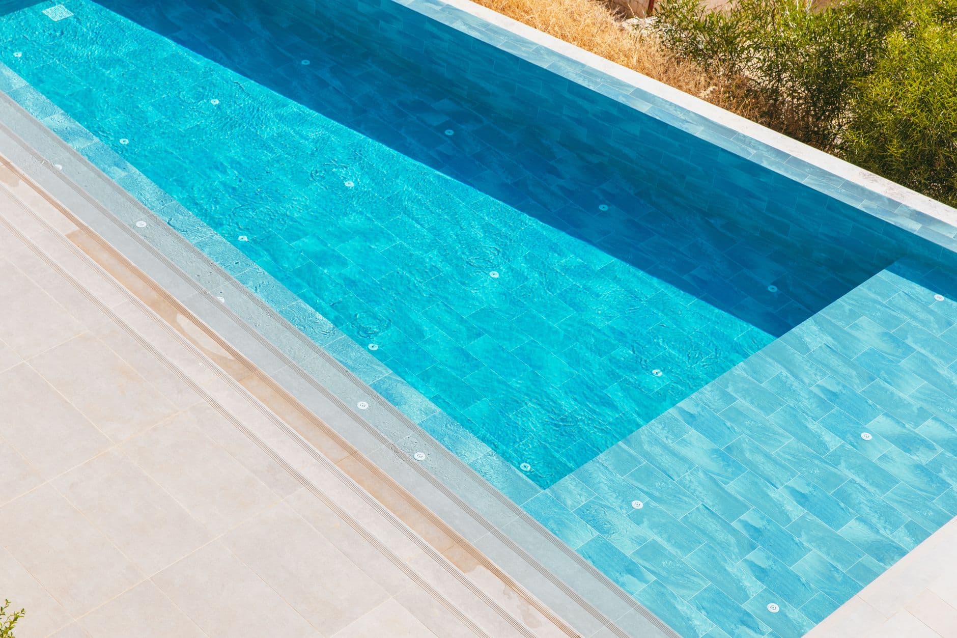 A rectangular swimming pool finished in blue tiling, with a tiled step run and a pale stone deck.