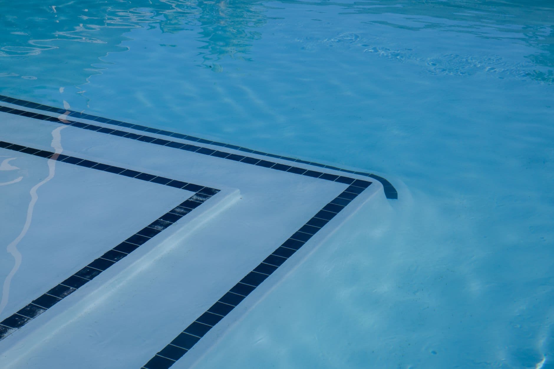 Submerged tiled steps in a swimming pool, each edged with a dark tile trim line beneath clear water.