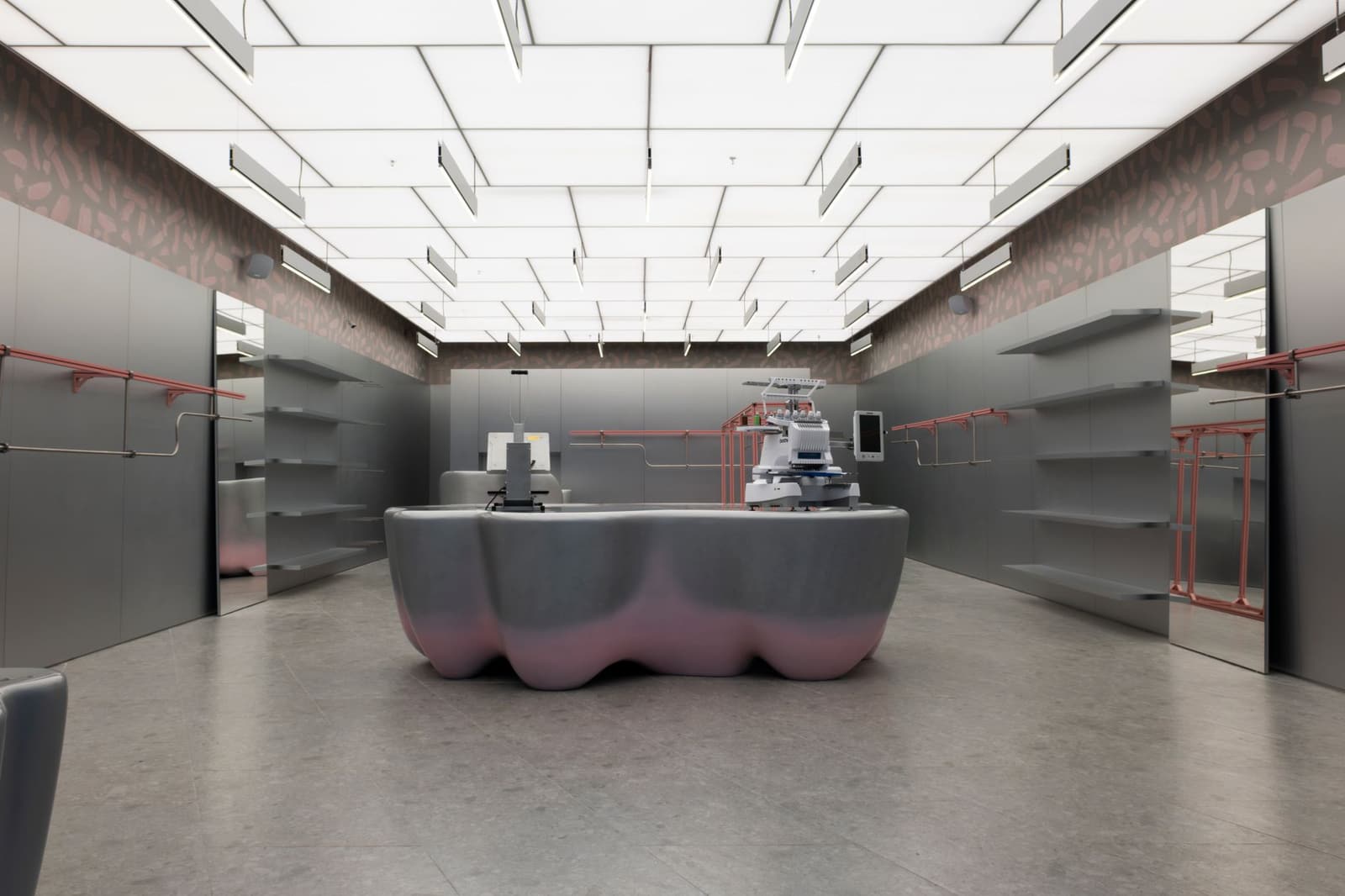An empty shop interior with grey wall shelving, clothes rails, a lit ceiling and a sculpted central counter.