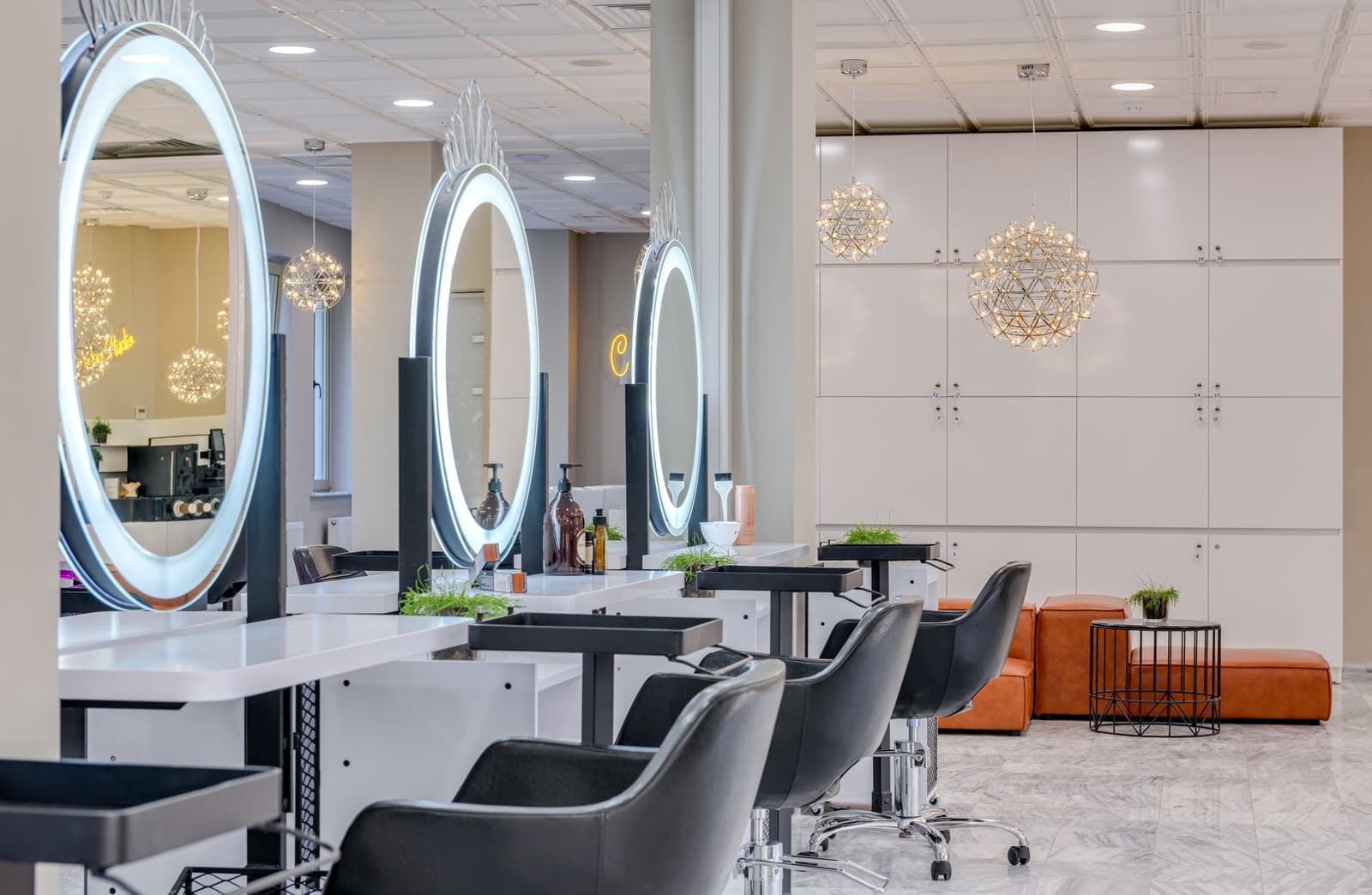 An empty hair salon with round illuminated mirrors, styling stations and white cabinetry.