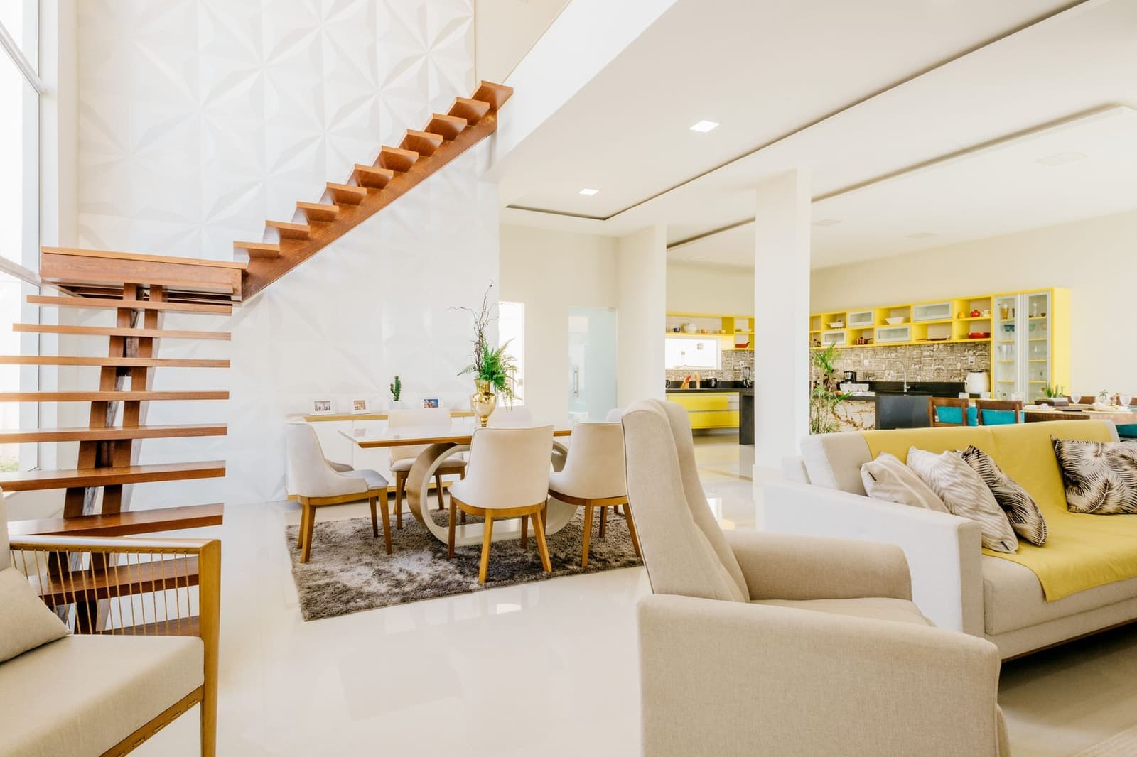 A bright open-plan living and dining area with white floors and an open timber staircase.
