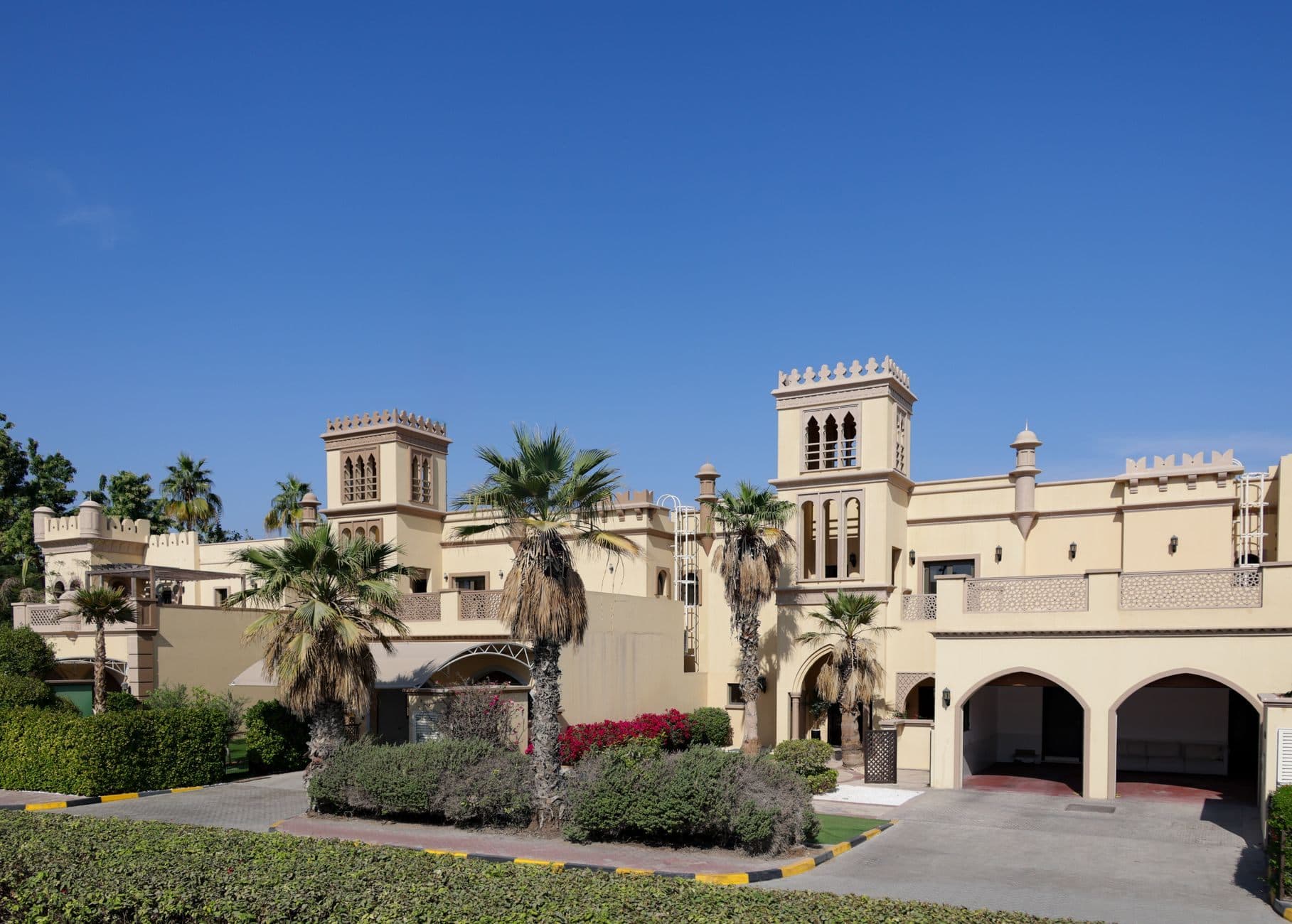 A sand-coloured villa with carved window screens, palm trees and an arched carport.